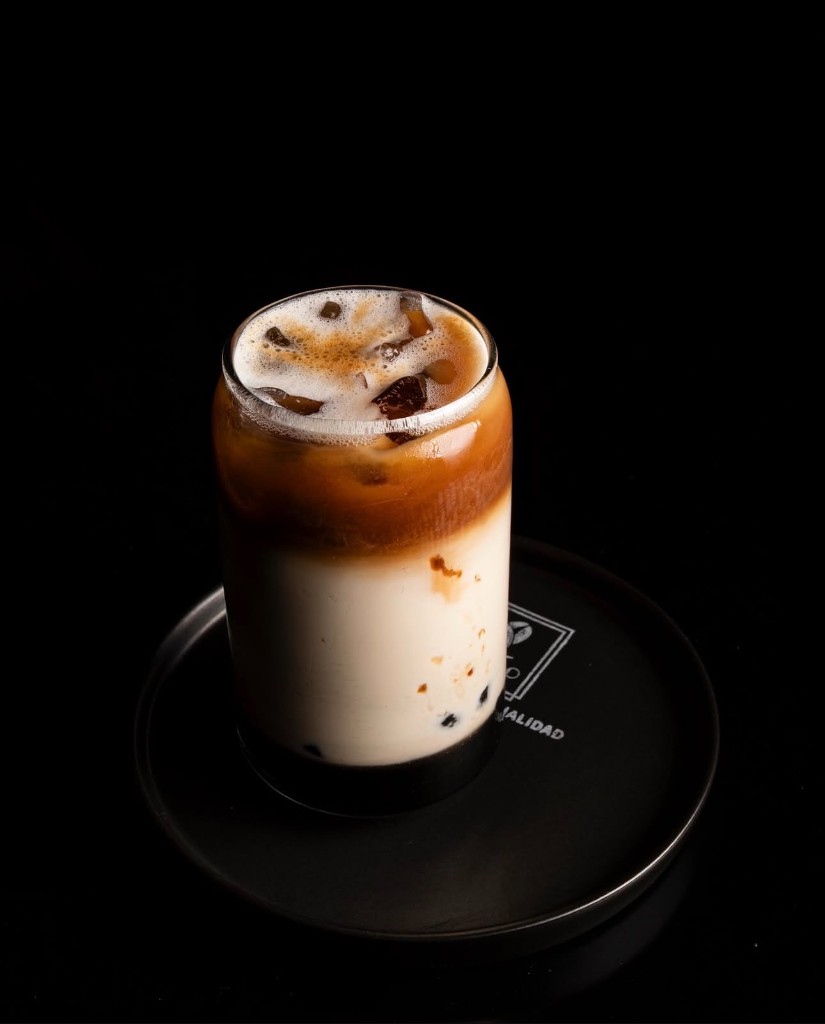 Café helado en capas en vaso de cristal, fondo oscuro.
