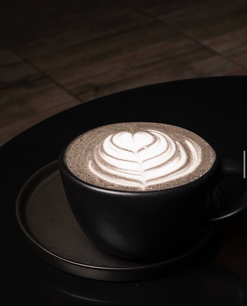 Latte oscuro en taza negra mate con arte latte, luz dramática.