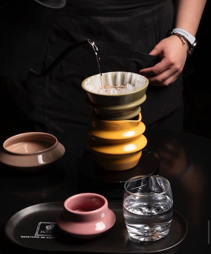 Barista preparando pour-over con goteador verde y jarra amarilla sobre báscula.