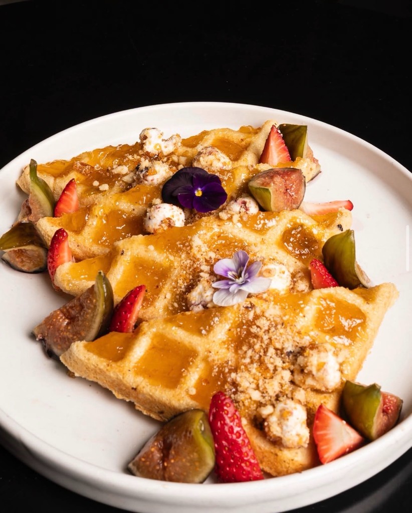 Waffles con higos, fresas, miel y flores comestibles en plato artesanal.
