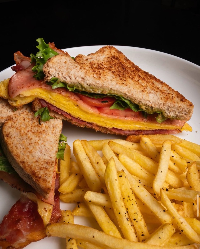 Sándwich club tostado con papas a la francesa en plato blanco.